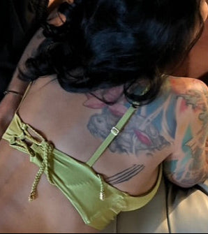A person wearing a yellow knot front twist bikini top with braided adjustable straps and a lace-up detail with braid and gold beads on the back.